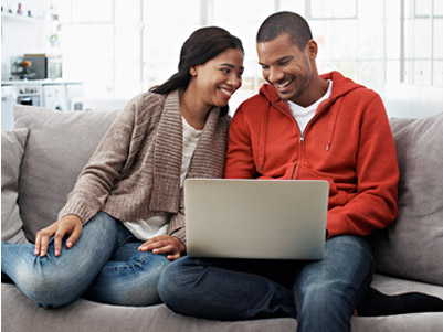 Young couple sitting together on the couch reviewing their bank statements on a laptop