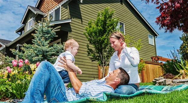 Cute couple laying on a blanket with their new baby in their front yard.
