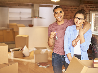 a young couple unpack their belongings as they settle into their new loft apartment . They are hugging and looking to camera smiling holding their keys aloft