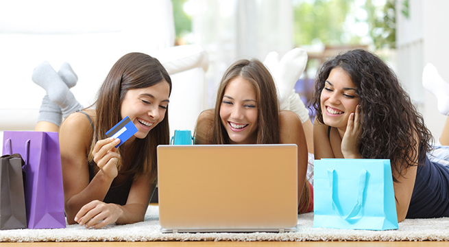 Three friends shopping online with credit card and laptop lying on the floor at home
