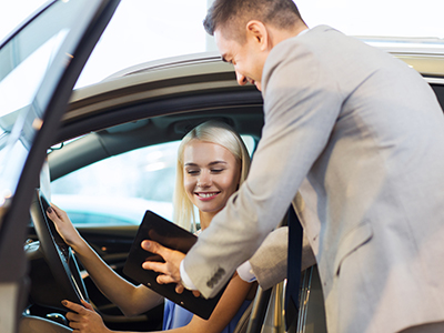 happy woman with car dealer in auto show or salon