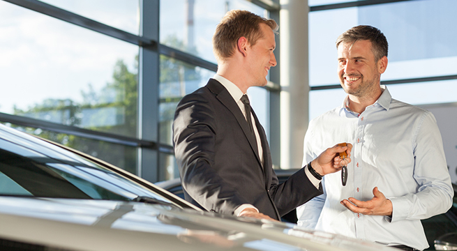 Car dealer handing keys to handsome male customer